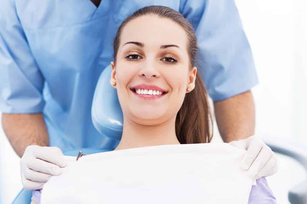 a woman sitting on a dental unit and the dentist standing behind her