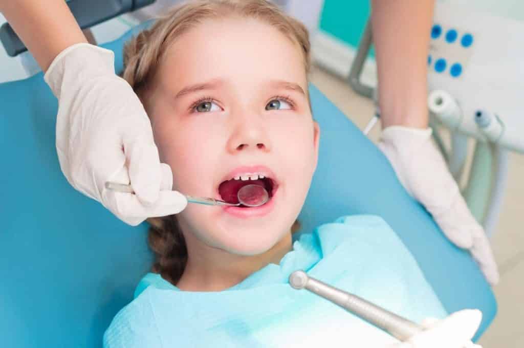 a baby girl sitting on dental unit while dentist is examining her